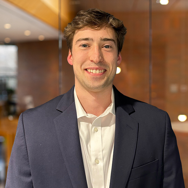 Smiling man in a navy blazer and white shirt, posing in a modern office setting.